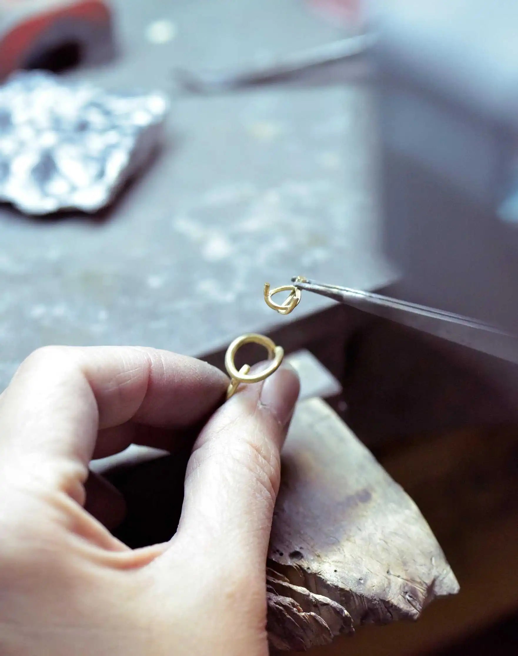 A craftsman assembles the Floating Pear Icon ring at Okker & Ockers, carefully placing a gold setting with fine tweezers.