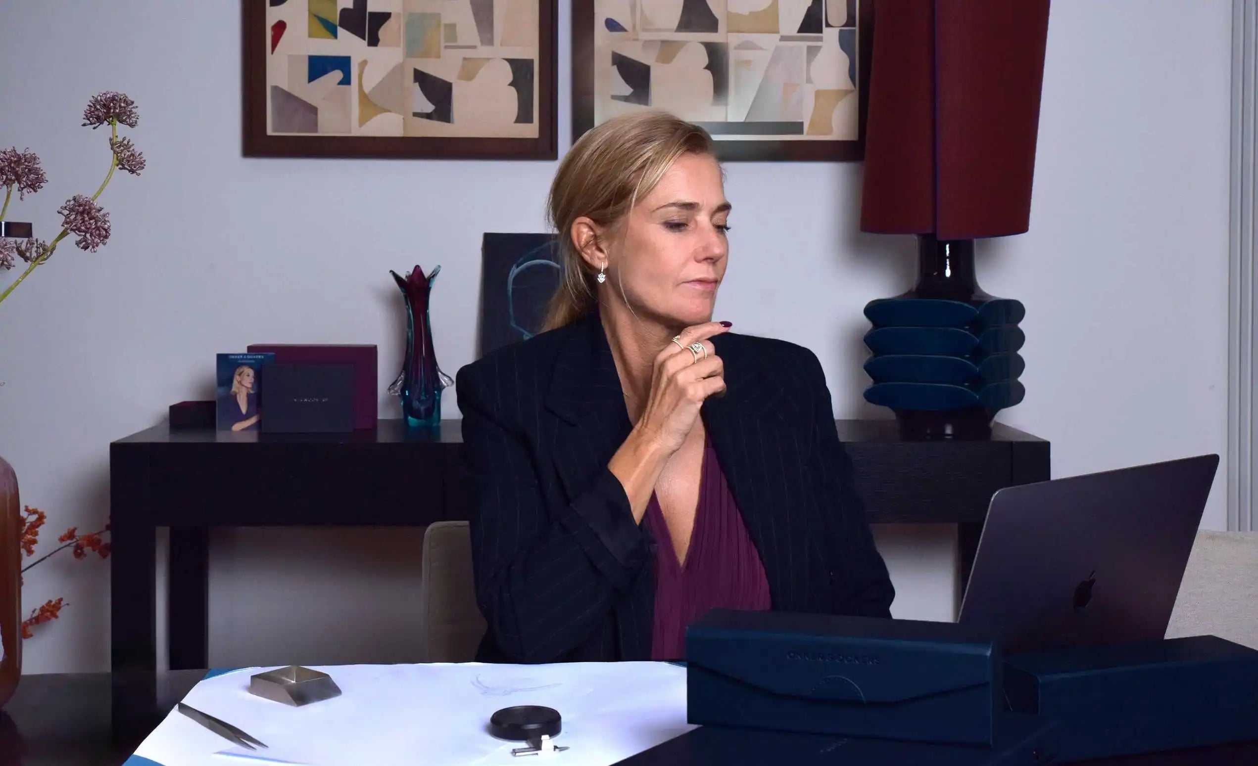 Susan Ockers during a consultation for custom rings, seated at a design table with Okker & Ockers packaging, sketches, and jewellery tools.