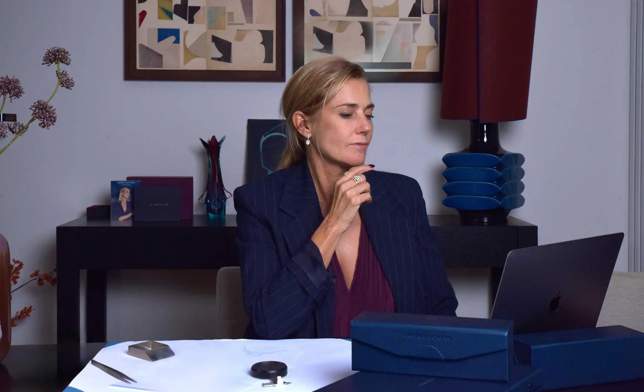Susan Ockers during a consultation for custom rings, seated at a design table with Okker & Ockers packaging, sketches, and jewellery tools. She wears elegant diamond rings and earrings, reflecting the craftsmanship and personalisation behind bespoke jewellery.