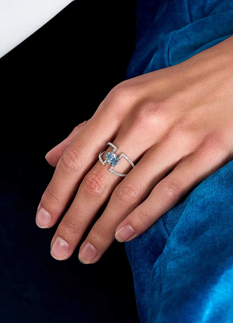 Close-up of model’s hand wearing the Entre-Blue ring in white gold, featuring a 1.2ct blue oval diamond, styled with a blue outfit.