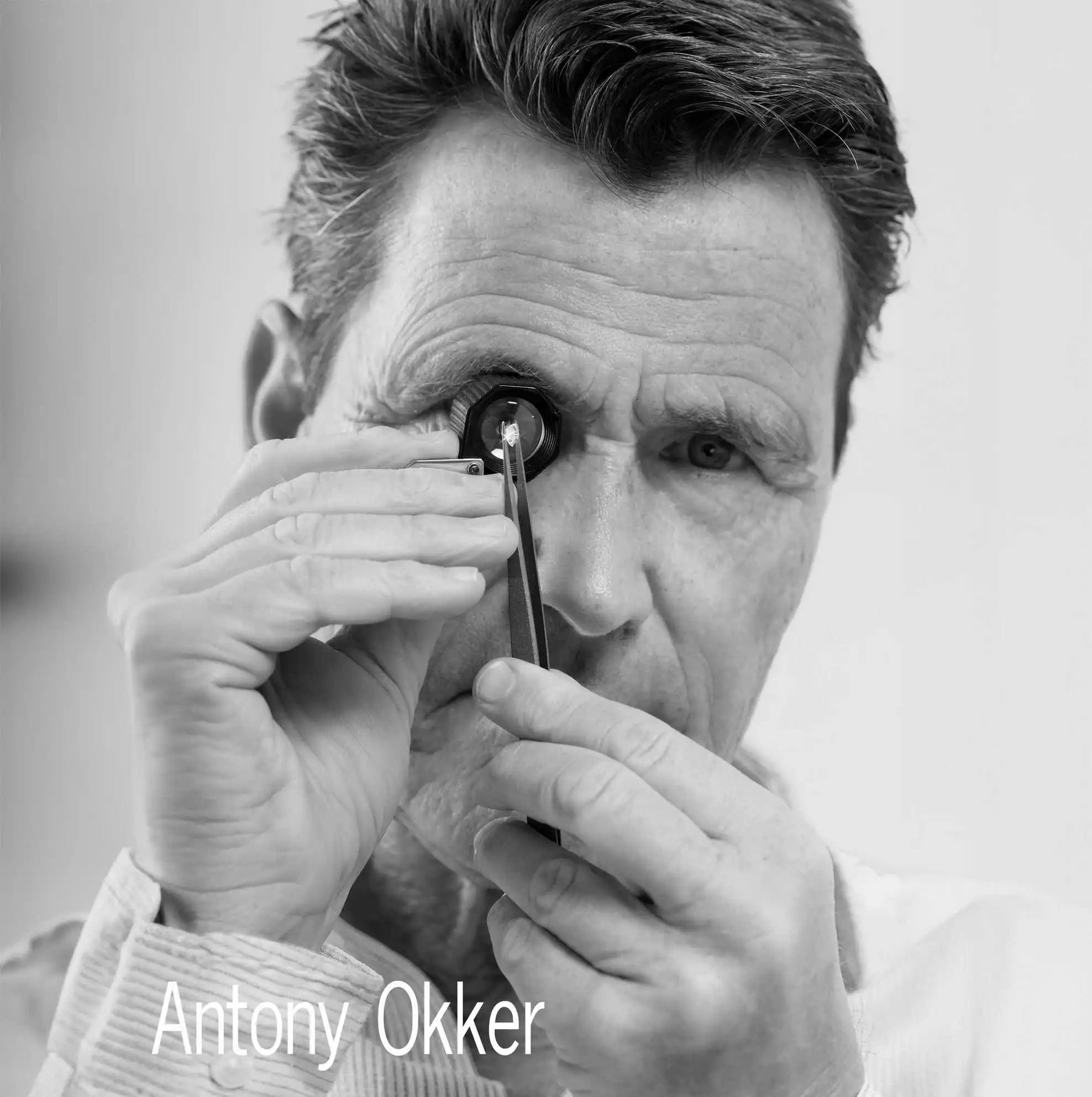 Antony Okker examining a lab-grown diamond through a loupe, holding the gem with precision tweezers.