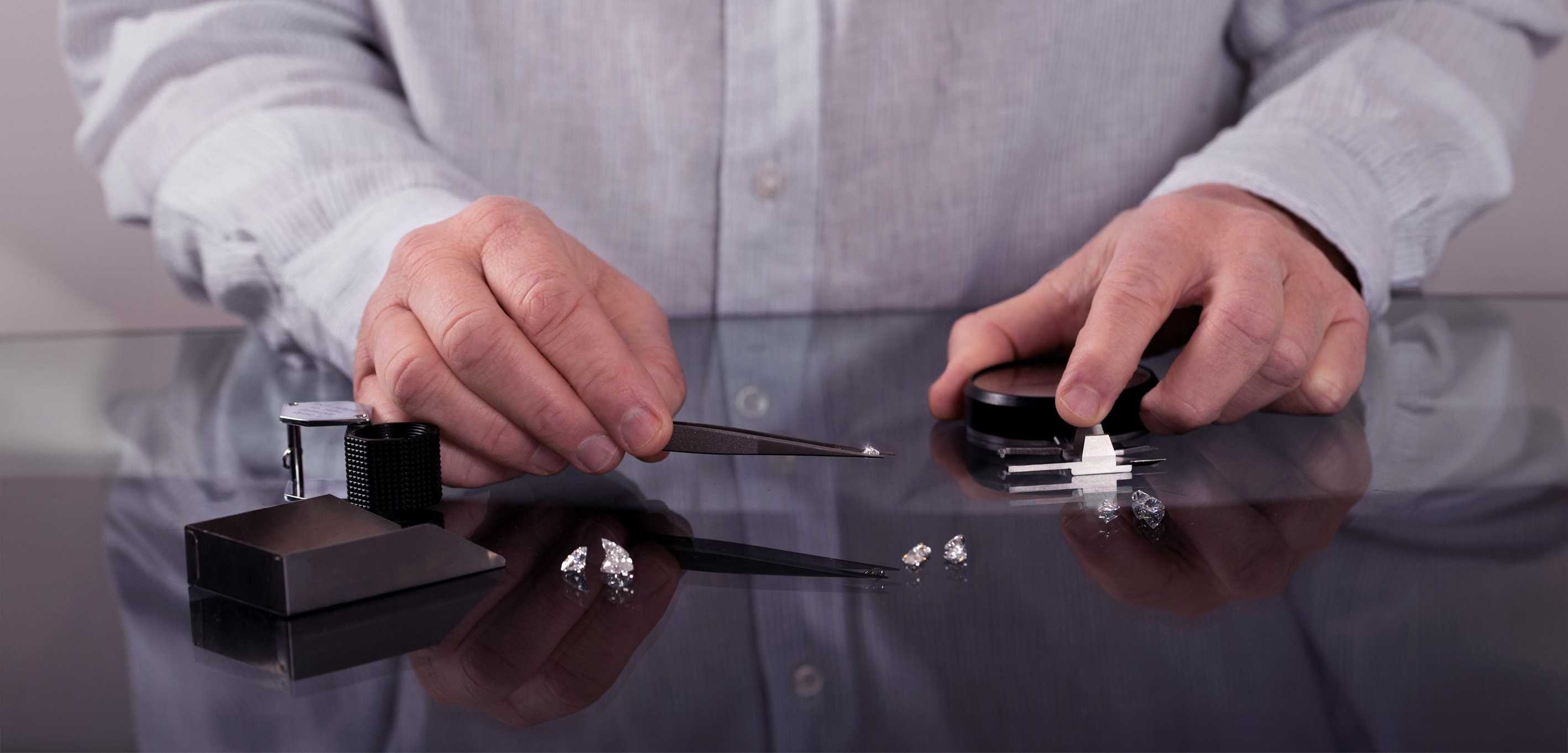 A gemologist examining and sorting loose lab-grown diamonds using precision tweezers, a loupe, and a diamond gauge.