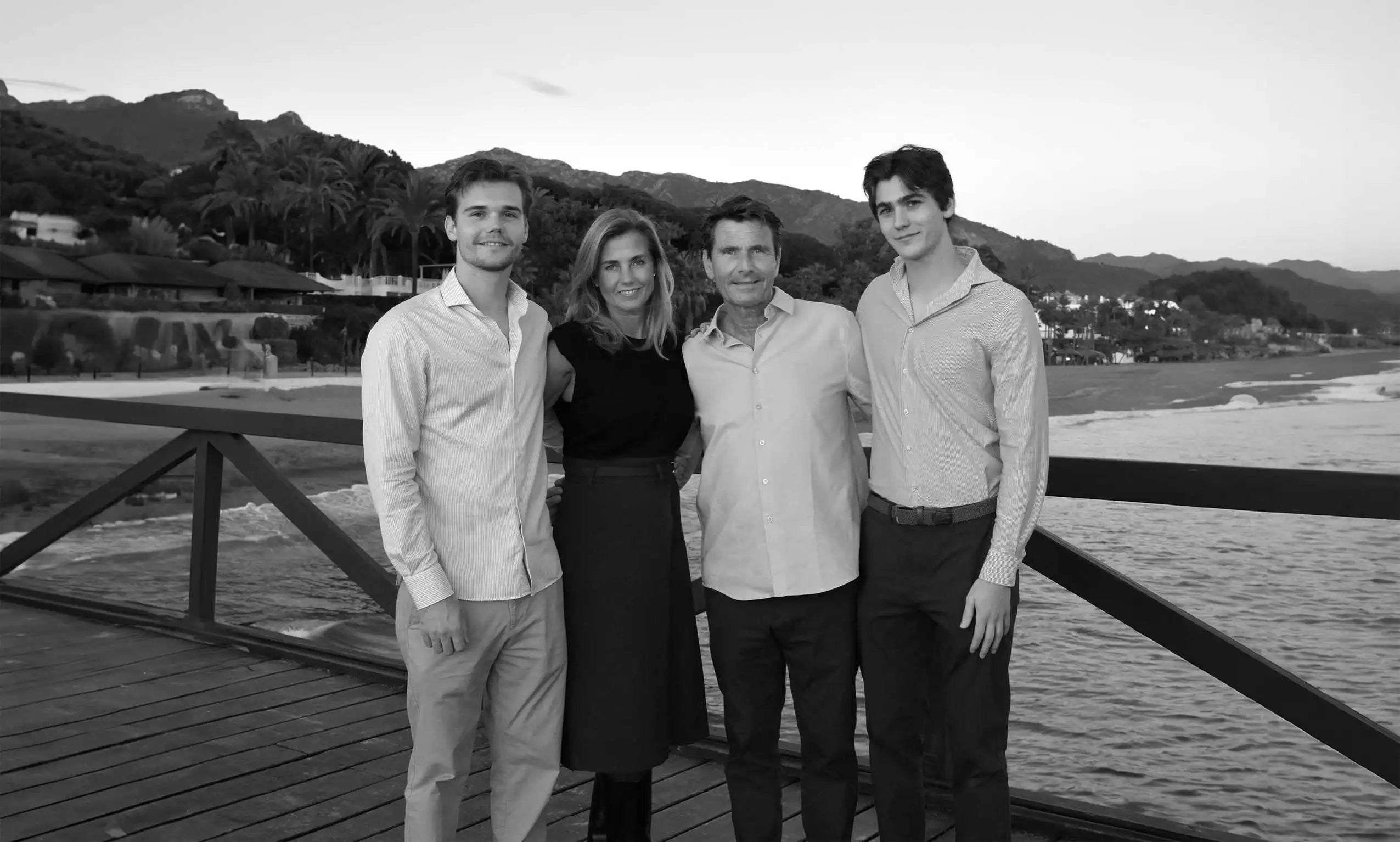 Black and white image of the Okker & Ockers family posing together on a wooden pier by the beach.