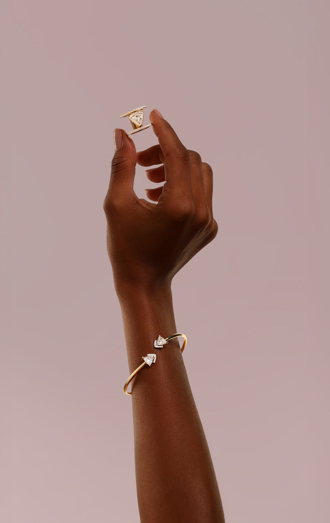 Hand holding a ring and wearing a bangle bracelet in gold and with two diamonds.