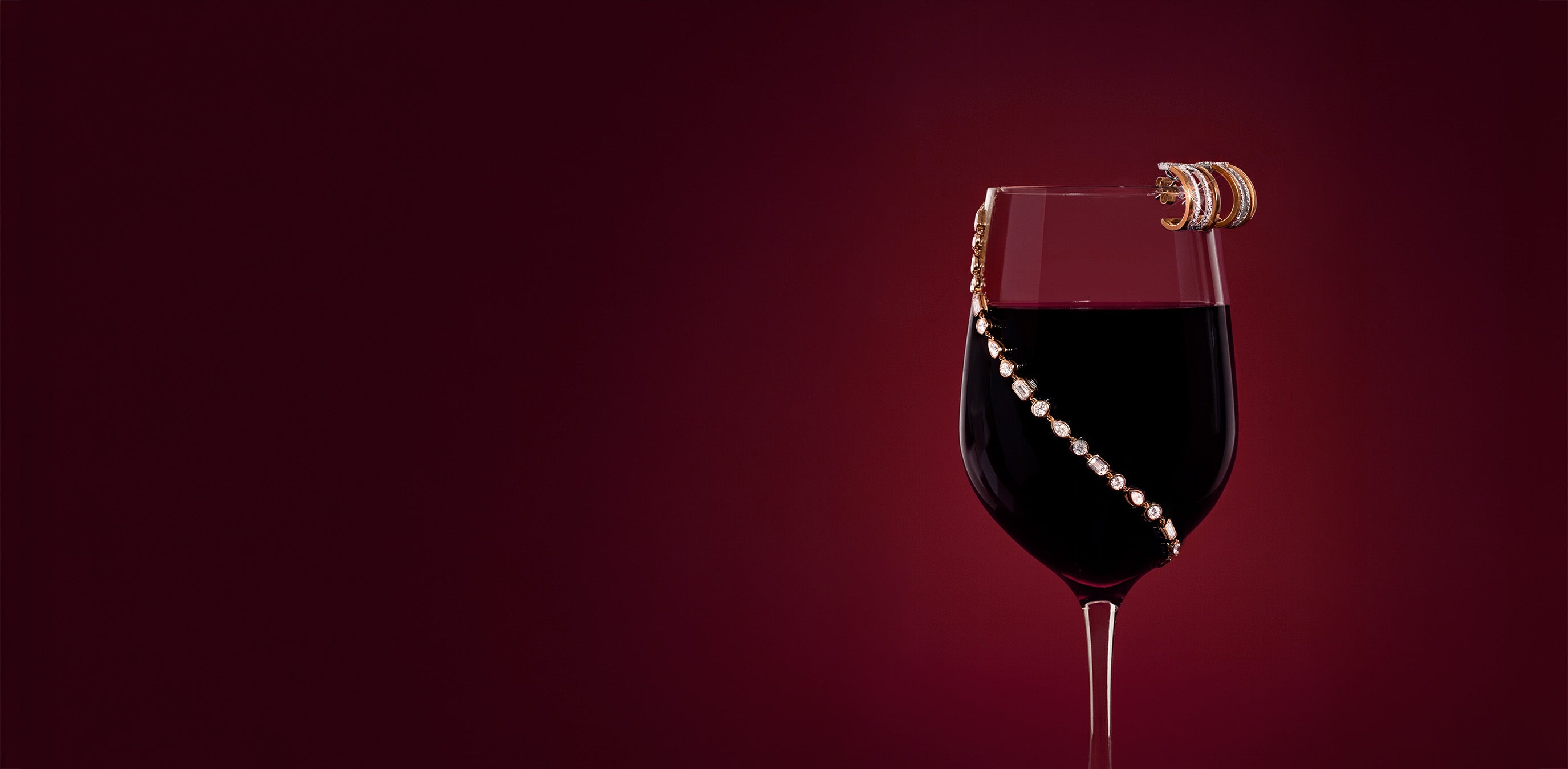 A classic tennis bracelet wrapped around a wine glass shot behind a red backdrop.