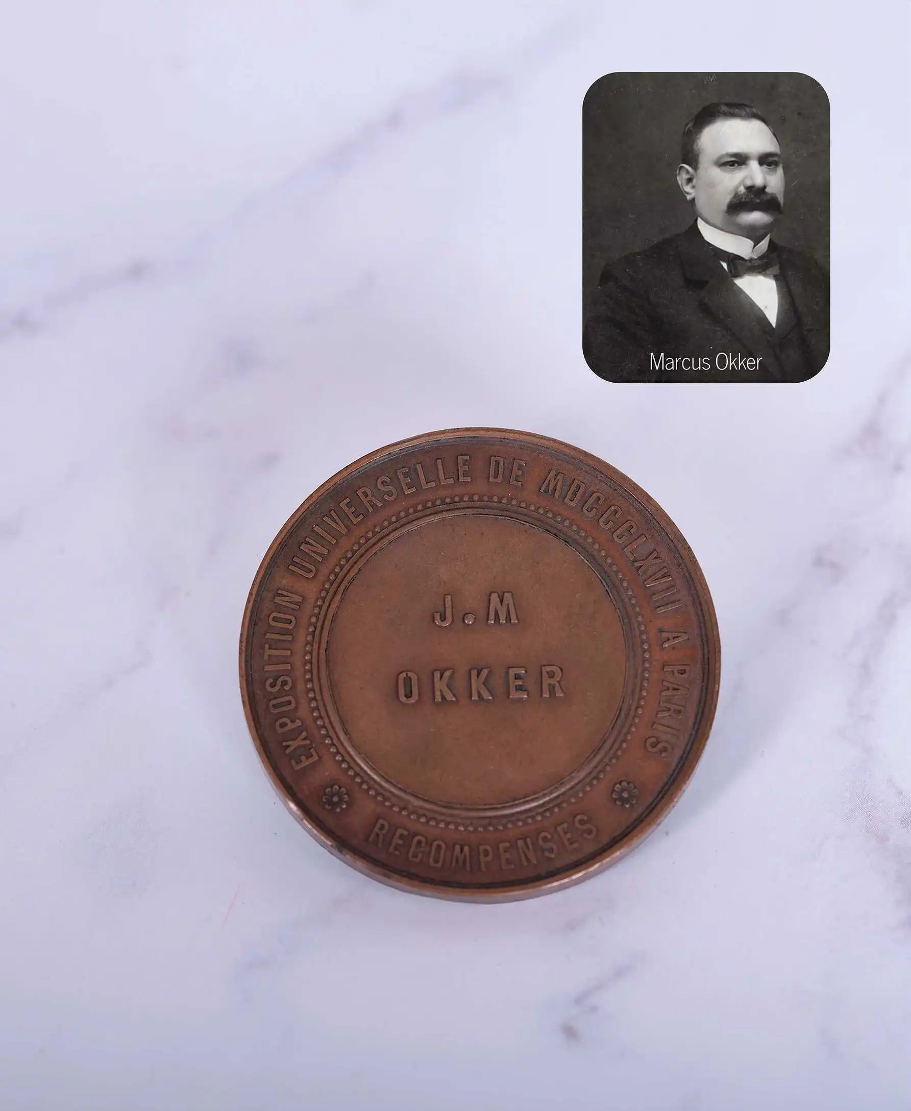 A historic bronze medallion engraved with 'J.M. Okker' from the Exposition Universelle in Paris, alongside a portrait of Marcus Okker.