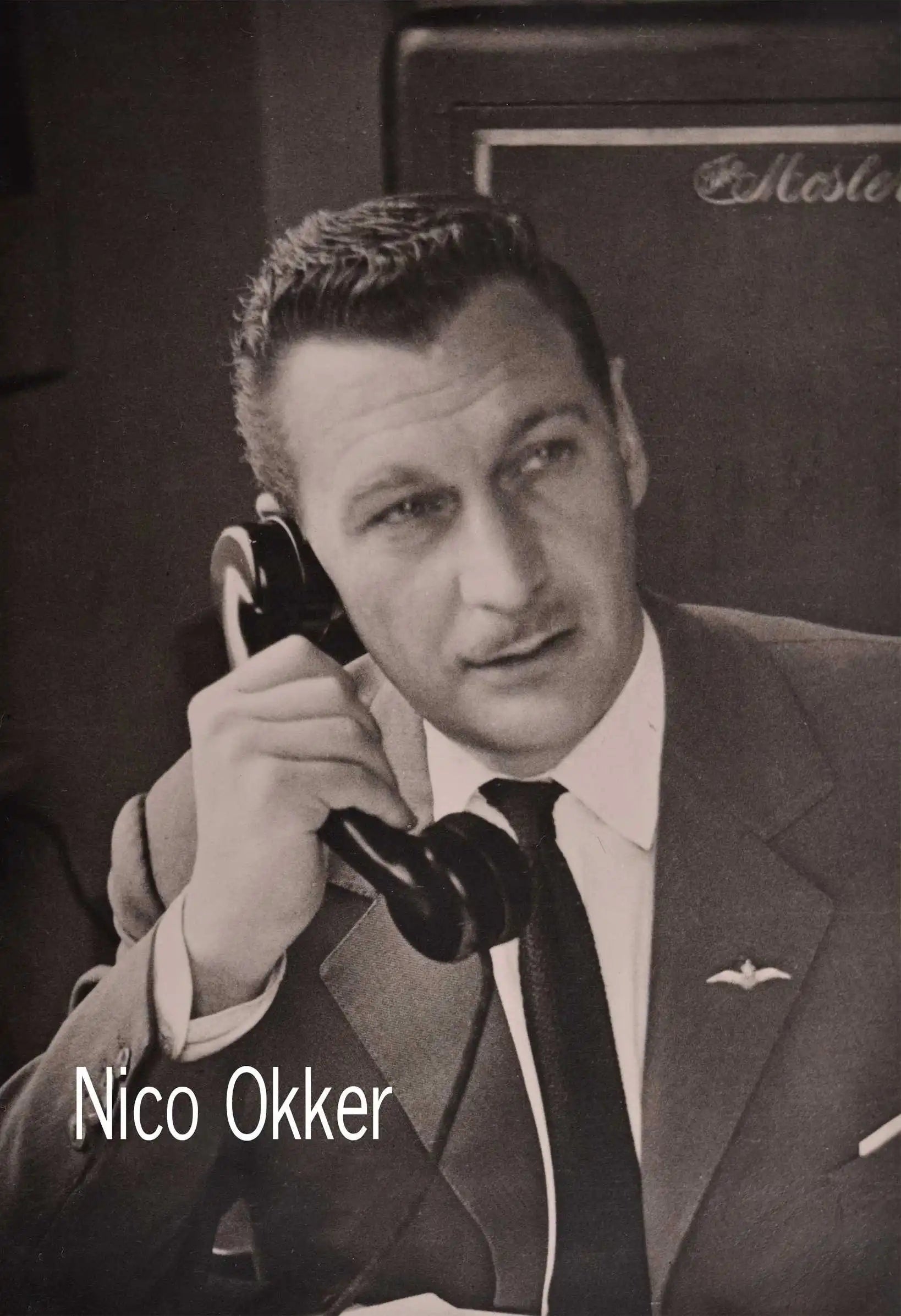 Black and white portrait of Nico Okker, dressed in a suit, holding a vintage telephone with a focused expression.