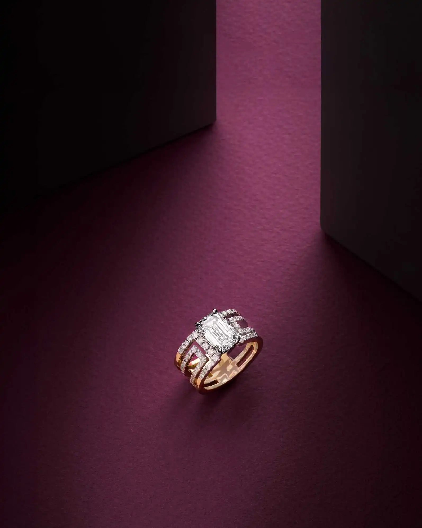 The yellow gold Heloise Emerald ring with a 3ct emerald diamond rests against an aubergine-coloured background.