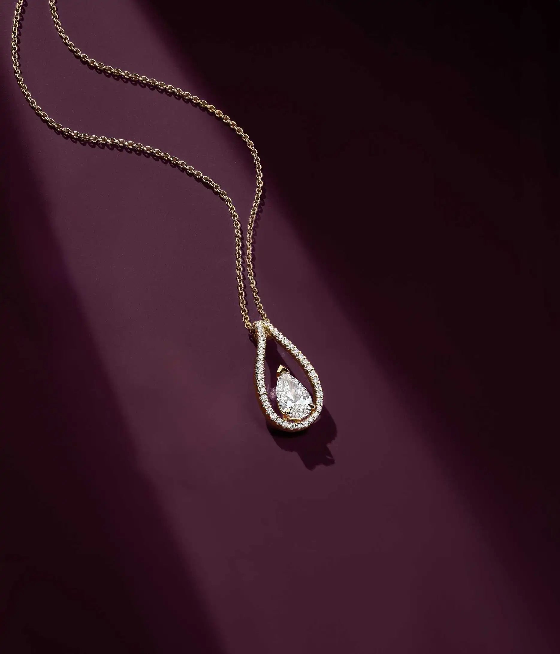 The lab-grown Floating Pear necklace set against an aubergine-coloured background, illuminated by a ray of light.