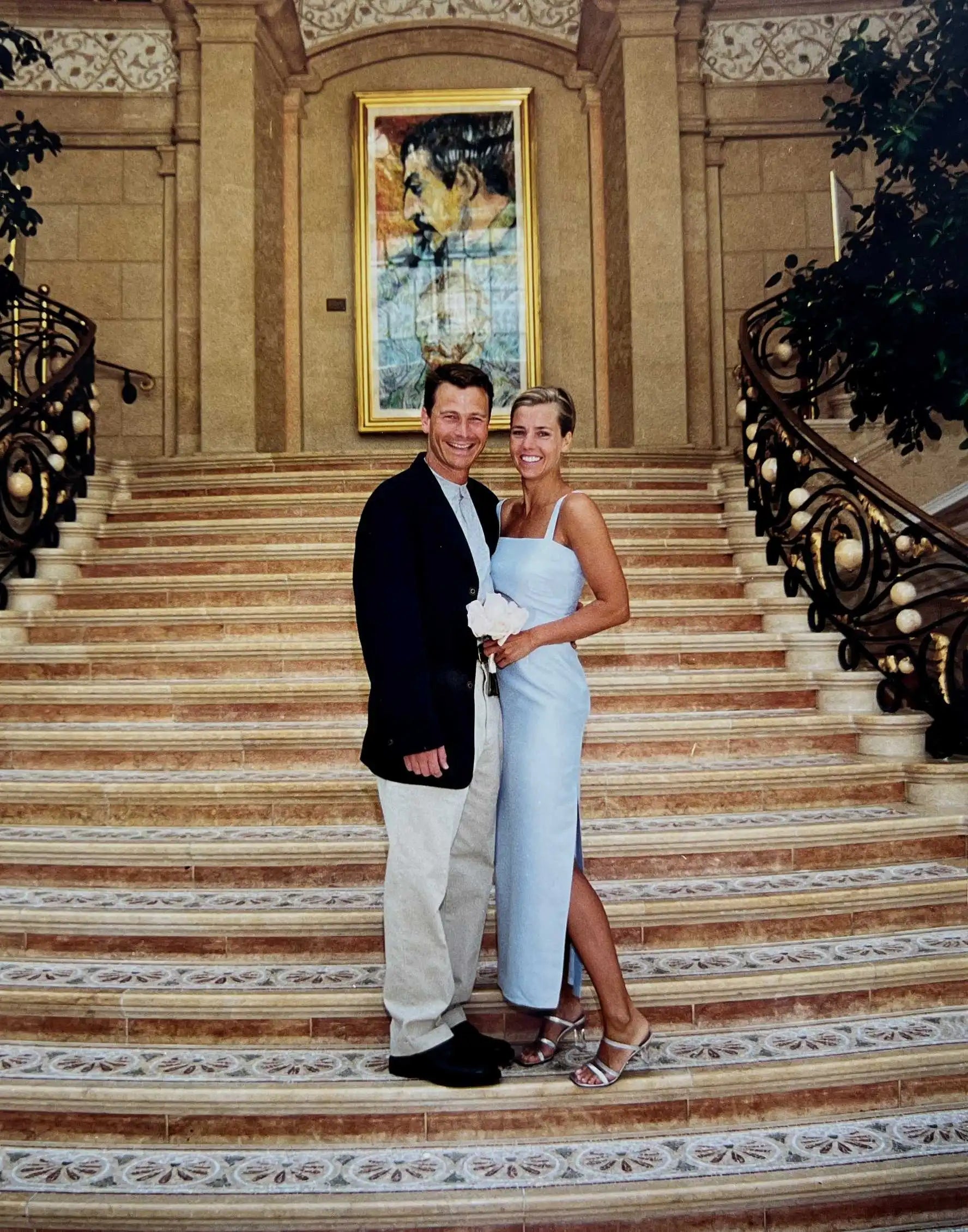 Susan Ockers and Antony Okker on their wedding day, posing on an ornate staircase.